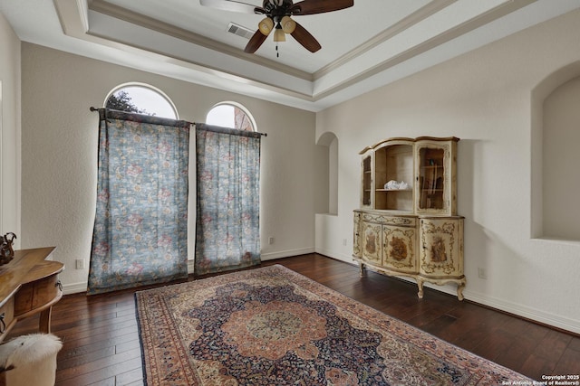 living area with ornamental molding, arched walkways, a raised ceiling, and hardwood / wood-style floors