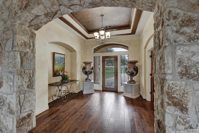 entryway with ornamental molding, a raised ceiling, wood-type flooring, and an inviting chandelier