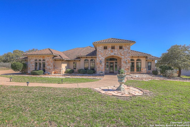 mediterranean / spanish-style home featuring french doors, a tile roof, stucco siding, stone siding, and a front lawn