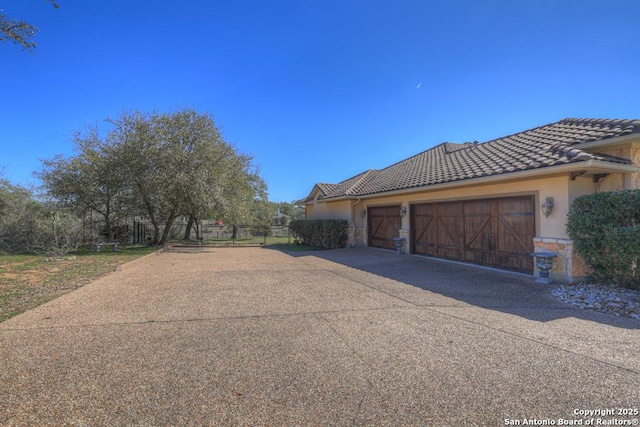 view of side of home featuring a garage, stone siding, a tile roof, and stucco siding