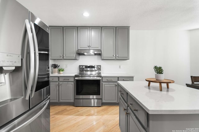 kitchen with a center island, stainless steel appliances, gray cabinets, light wood-style flooring, and under cabinet range hood