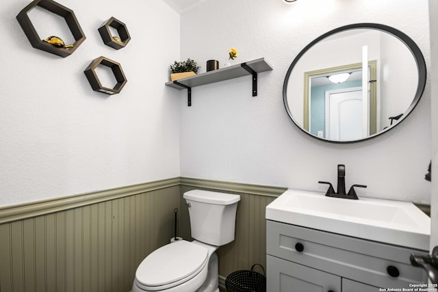 half bath with toilet, a wainscoted wall, and vanity