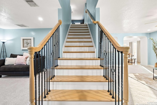 stairway with a textured ceiling, visible vents, arched walkways, and carpet flooring