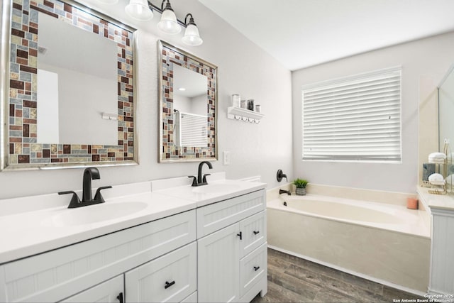 bathroom with wood finished floors, a garden tub, a sink, and double vanity