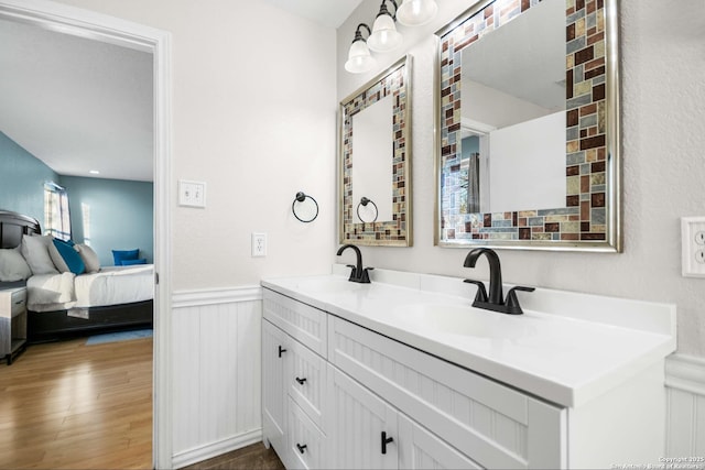 ensuite bathroom featuring ensuite bathroom, wood finished floors, a sink, wainscoting, and double vanity