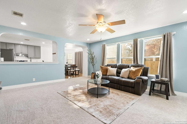 living room featuring arched walkways, a textured ceiling, light carpet, visible vents, and baseboards