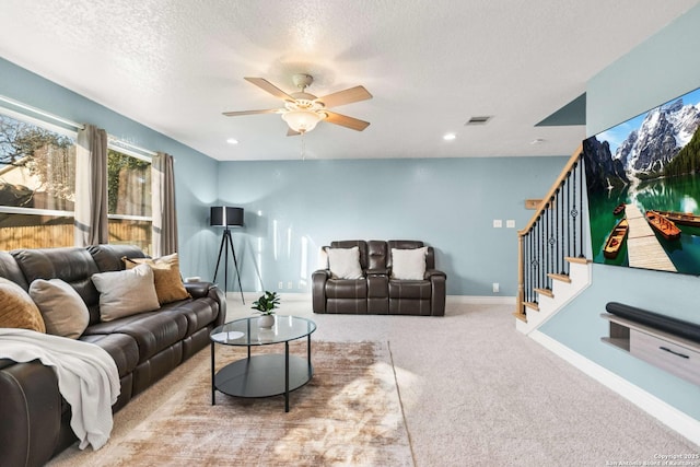 living room with baseboards, light colored carpet, ceiling fan, stairway, and a textured ceiling