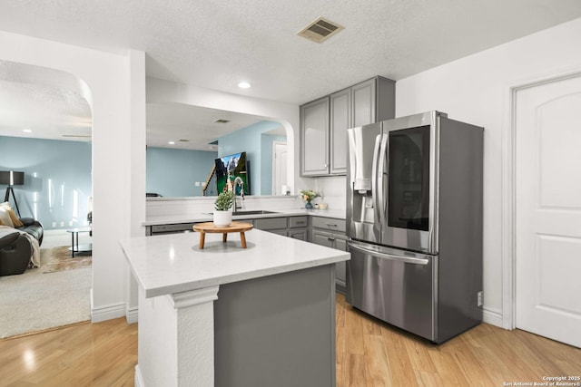 kitchen with arched walkways, a center island, light wood finished floors, gray cabinets, and smart refrigerator