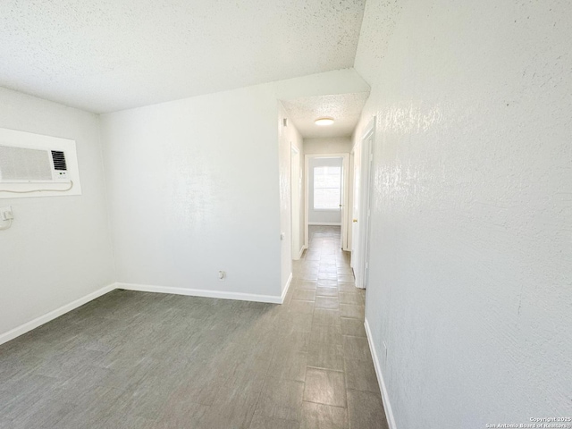 interior space featuring baseboards, dark wood-style flooring, a textured ceiling, and a wall mounted AC