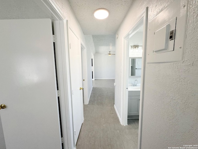 hallway featuring a textured ceiling, electric panel, a sink, and a textured wall