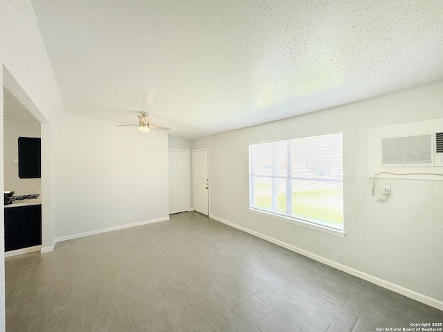 empty room with ceiling fan, baseboards, a textured ceiling, and a wall mounted air conditioner