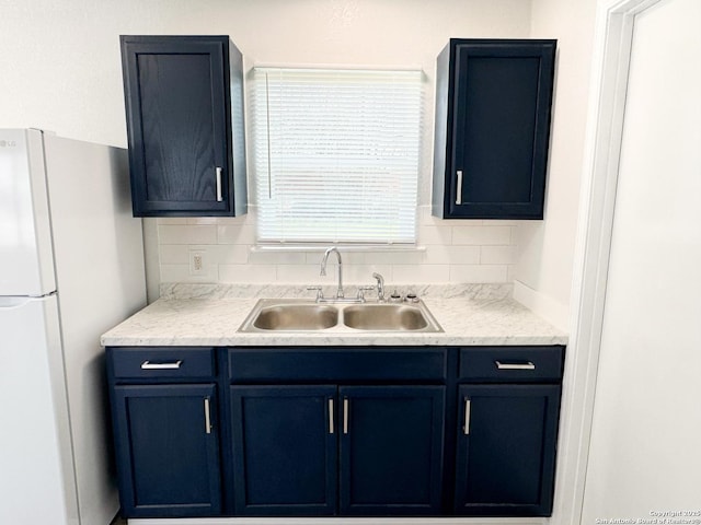 kitchen featuring light countertops, tasteful backsplash, a sink, and freestanding refrigerator