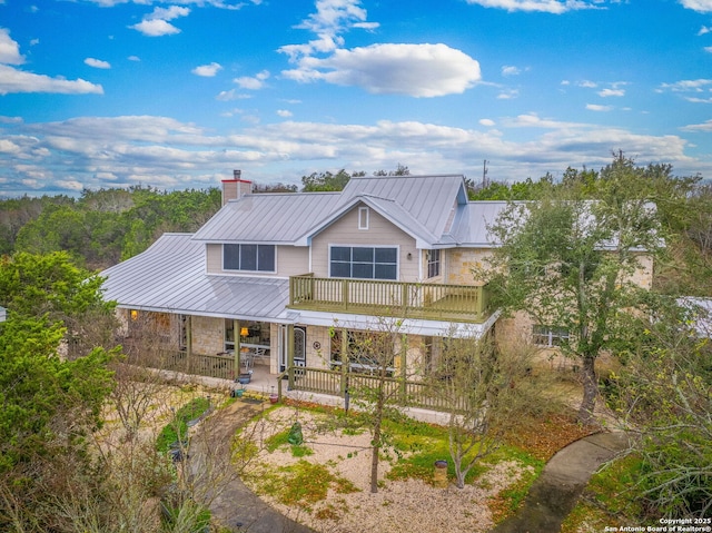 rear view of property featuring a balcony, stone siding, a fenced front yard, metal roof, and a standing seam roof