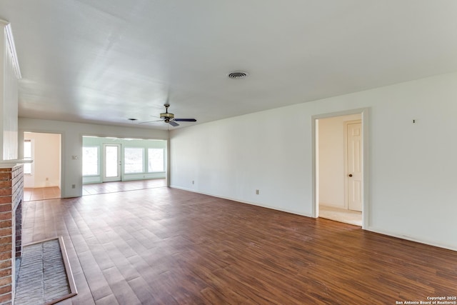 unfurnished living room featuring visible vents, baseboards, a ceiling fan, a brick fireplace, and dark wood finished floors