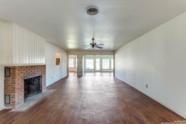 unfurnished living room featuring ceiling fan, visible vents, baseboards, a brick fireplace, and dark wood finished floors