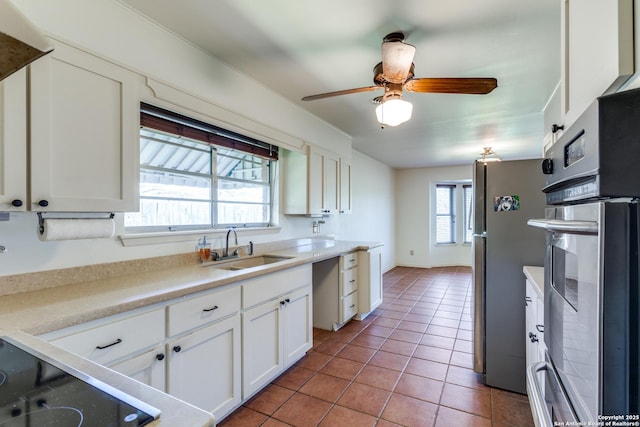 kitchen with light tile patterned floors, stainless steel appliances, light countertops, white cabinets, and a sink