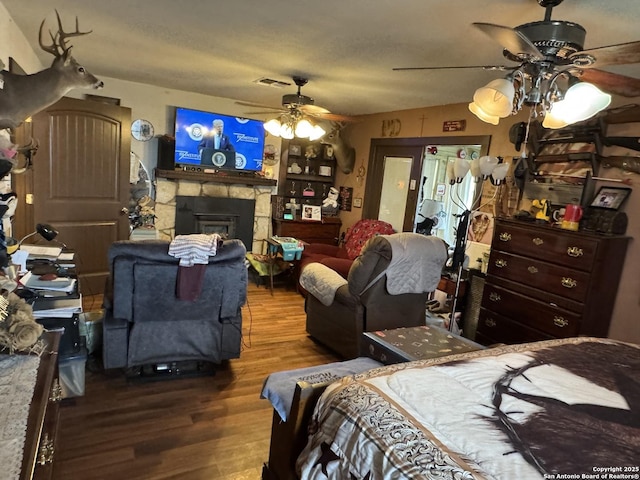 bedroom featuring a textured ceiling, a fireplace, wood finished floors, visible vents, and a ceiling fan