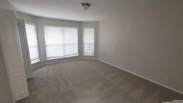 unfurnished room with dark carpet and baseboards