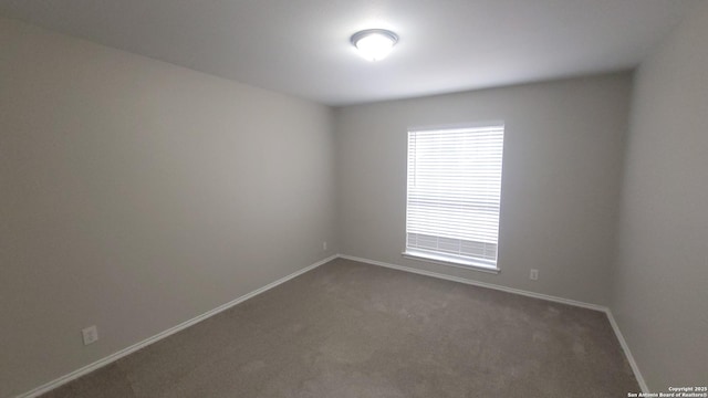 empty room featuring dark colored carpet and baseboards