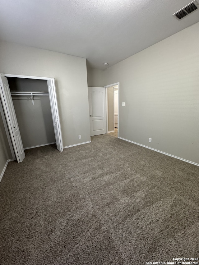 unfurnished bedroom with a closet, dark carpet, visible vents, and baseboards