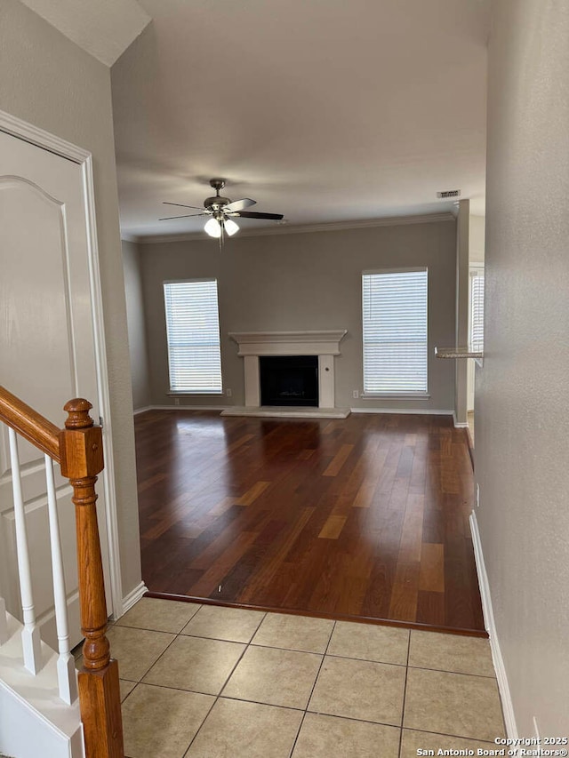 unfurnished living room featuring baseboards, a fireplace with raised hearth, ceiling fan, stairway, and light tile patterned flooring