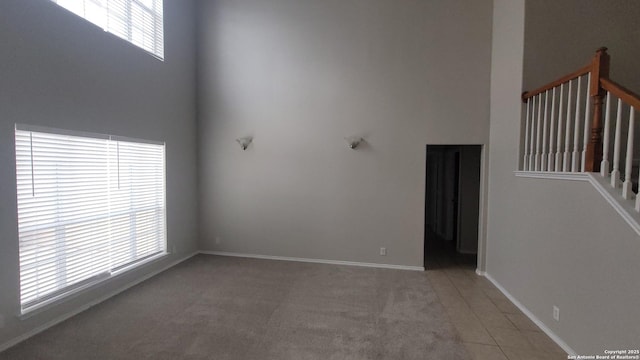 unfurnished living room with a towering ceiling, carpet, stairway, and baseboards