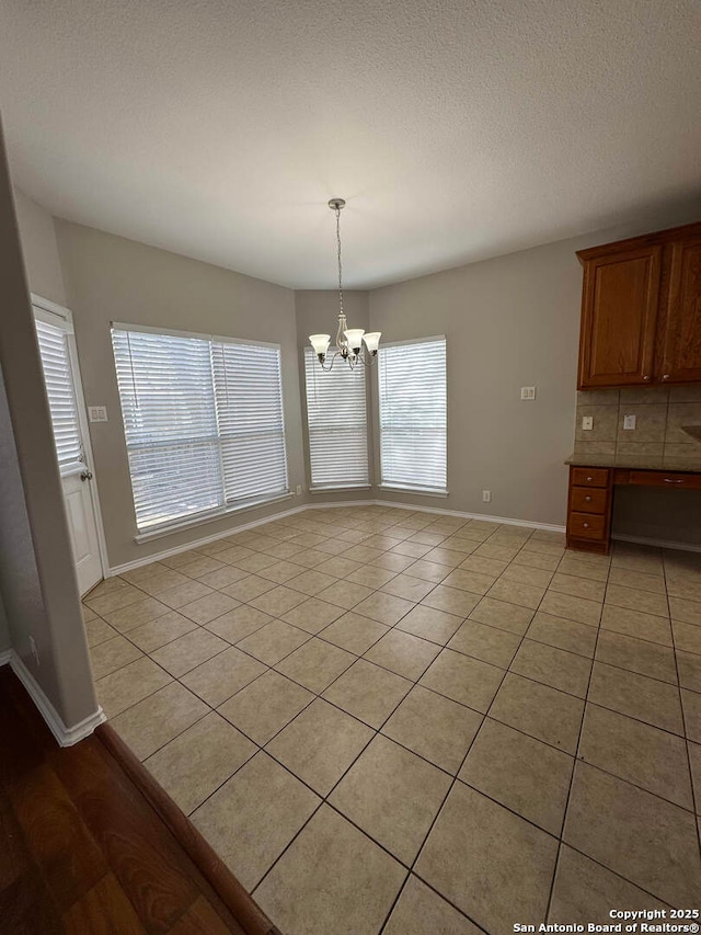 unfurnished dining area with a textured ceiling, light tile patterned flooring, baseboards, built in study area, and an inviting chandelier