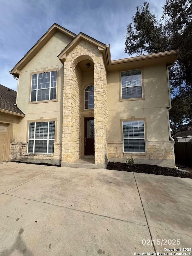 traditional home featuring stone siding, driveway, and stucco siding