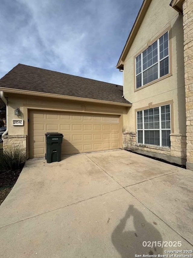 view of side of home with an attached garage, stone siding, a shingled roof, and concrete driveway