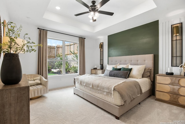 bedroom featuring light carpet, ceiling fan, and a tray ceiling