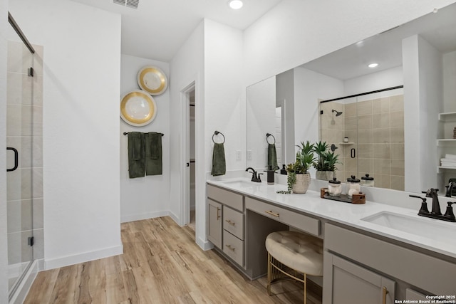 bathroom with double vanity, a shower stall, a sink, and wood finished floors