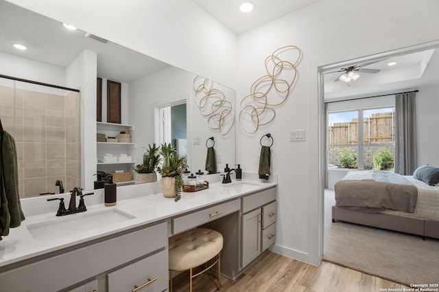 ensuite bathroom with double vanity, ensuite bath, a sink, and wood finished floors