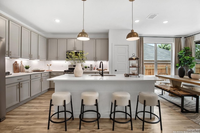 kitchen featuring light countertops, a sink, decorative light fixtures, and a center island with sink