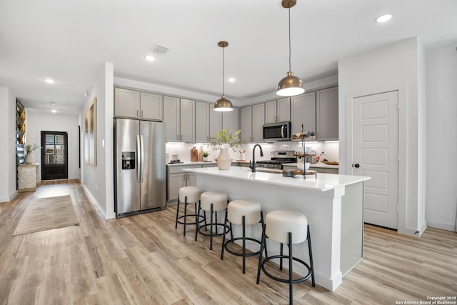 kitchen featuring stainless steel appliances, a kitchen island with sink, gray cabinets, and light countertops