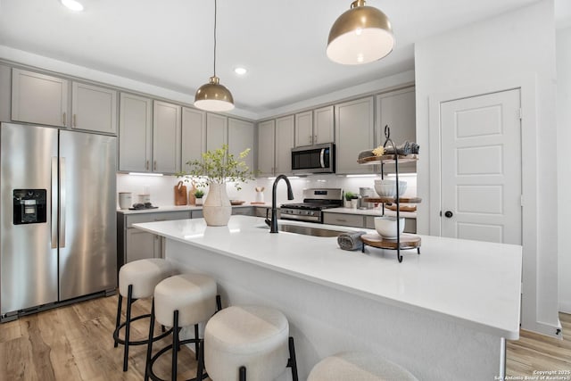 kitchen featuring an island with sink, appliances with stainless steel finishes, light countertops, and hanging light fixtures