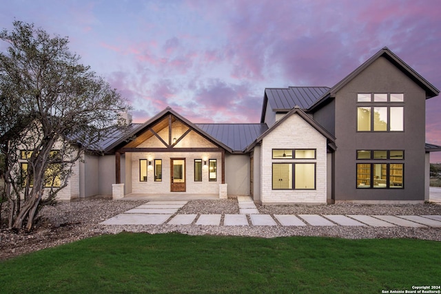 back of house with stone siding, metal roof, a standing seam roof, a yard, and stucco siding