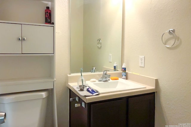 half bath featuring toilet, a textured wall, and vanity