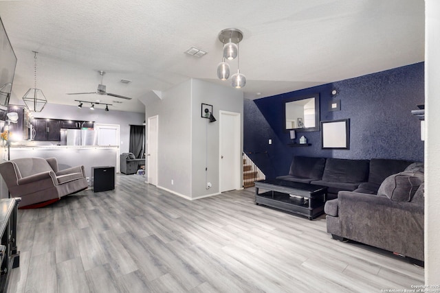 living room featuring visible vents, stairway, light wood-style floors, a ceiling fan, and a textured ceiling