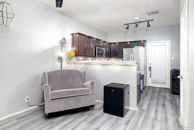 kitchen featuring dark brown cabinetry, visible vents, stainless steel microwave, a peninsula, and light countertops