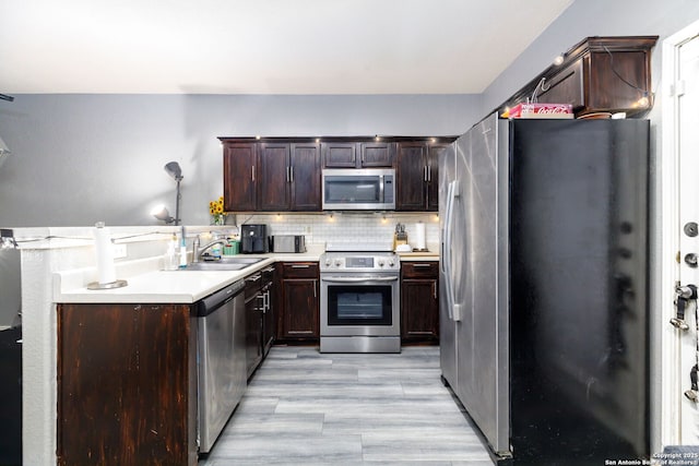 kitchen with a sink, light countertops, appliances with stainless steel finishes, light wood-type flooring, and decorative backsplash