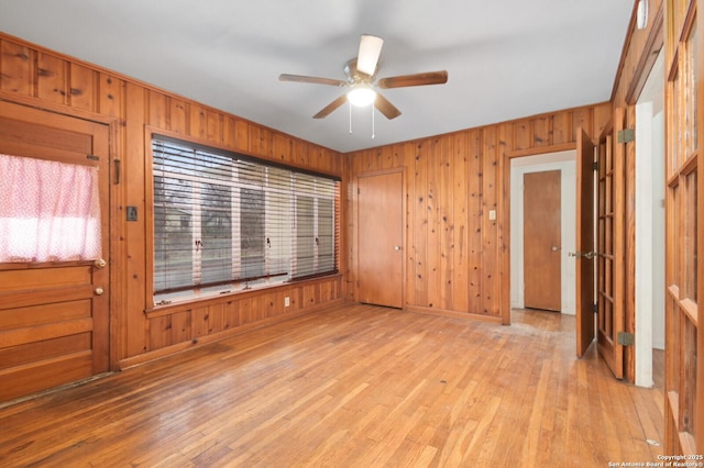 unfurnished room with light wood-type flooring, ceiling fan, wooden walls, and baseboards