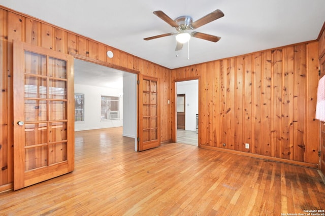 empty room featuring light wood-type flooring, wood walls, baseboards, and a ceiling fan