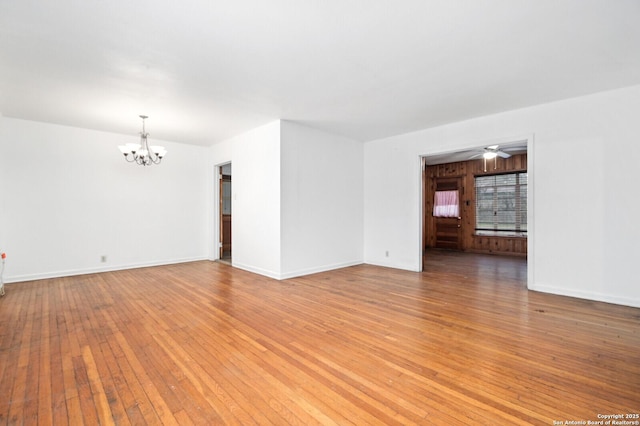 empty room with ceiling fan with notable chandelier, light wood-type flooring, and baseboards