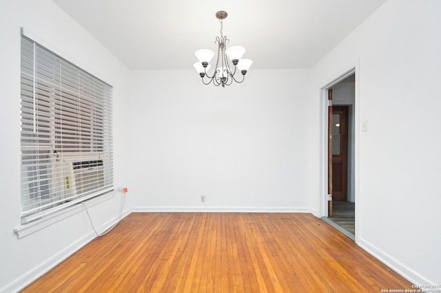 empty room with baseboards, a chandelier, and wood finished floors