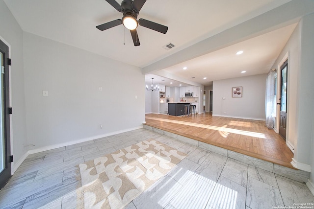 unfurnished living room featuring baseboards, ceiling fan with notable chandelier, visible vents, and recessed lighting