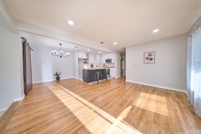 unfurnished living room with light wood-type flooring, baseboards, and a barn door