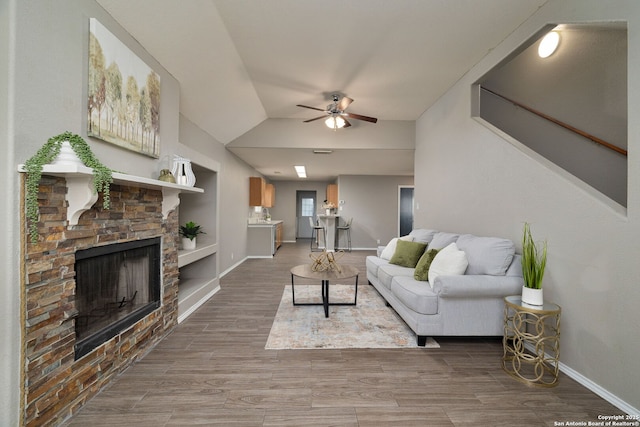 living area featuring baseboards, lofted ceiling, ceiling fan, wood finished floors, and a fireplace