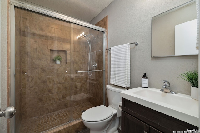 full bathroom featuring toilet, a stall shower, a textured wall, and vanity