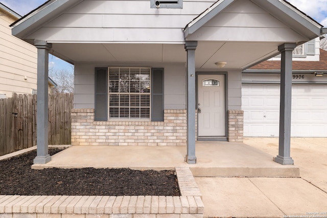 property entrance featuring a garage, concrete driveway, brick siding, and fence