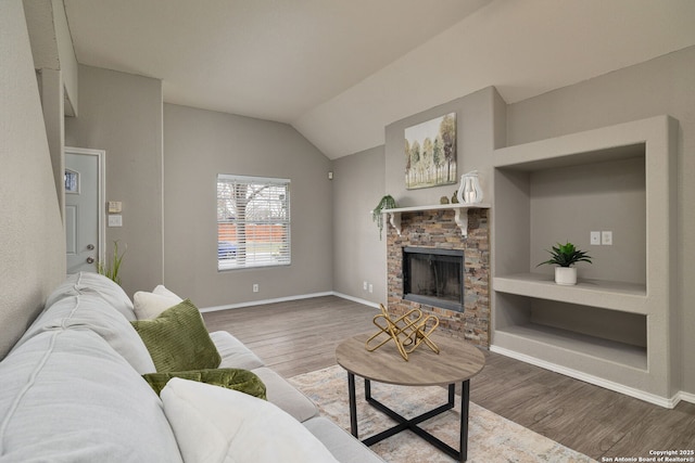 living room featuring lofted ceiling, a stone fireplace, dark wood-style flooring, built in features, and baseboards